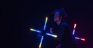 Photo en action pendant le show visuel lors d'une soirée d'entreprise à Lyon. L'artiste manipule un grand bâton lumineux (staff) dont les extrémités dessinent des cercles parfaits sur une place publique en extérieur.